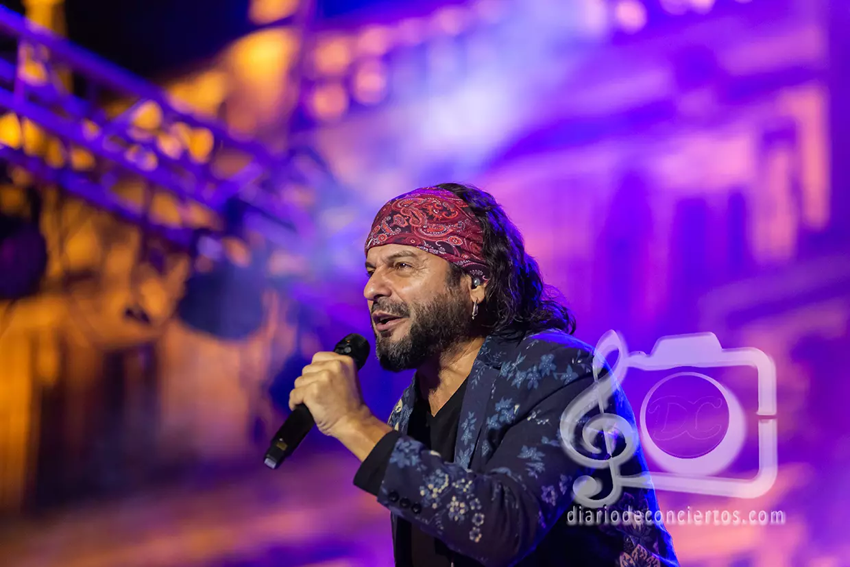 El Arrebato cantando en directo con un micrófono en el escenario de la Plaza Mayor de Salamanca, vistiendo una chaqueta azul estampada y un pañuelo bandana en la cabeza.