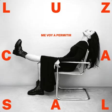 Portada del disco "Me voy a permitir" de Luz Casal, donde aparece la artista sentada en una silla de diseño, vestida de negro sobre un fondo blanco con letras rojas.