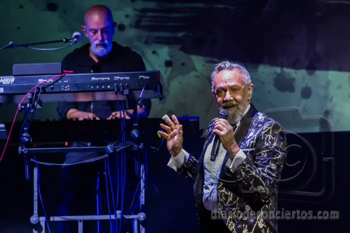 Rafa Sánchez cantando con un micrófono en el escenario del Teatro Liceo de Salamanca, vistiendo una americana estampada brillante, con un teclista calvo al fondo.