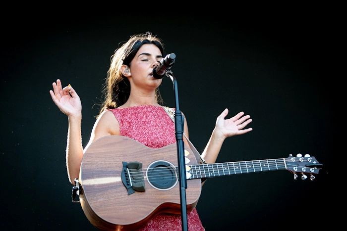 Mafalda Cardenal cantando en directo con micrófono y guitarra acústica sobre fondo negro en un festival.