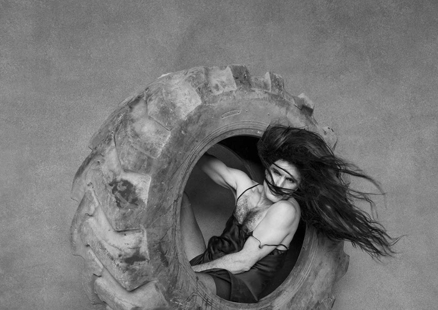 Rodrigo Cuevas en Salamanca. El artista Rodrigo Cuevas asomado dentro de una gran rueda de tractor en blanco y negro, imagen promocional de su gira La Belleza.