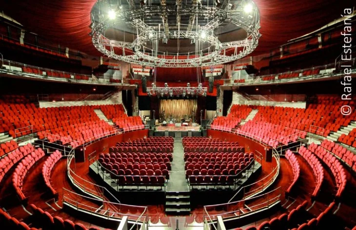 Vista panorámica del graderío circular con asientos rojos y la pista central del Teatro Circo Price en Madrid bajo una gran estructura de luces.